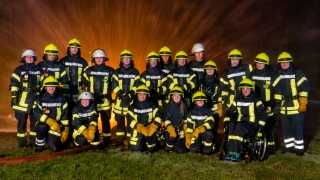 – Gruppenfoto der Lehrgangsteilnehmer während einer praktischen Ausbildungseinheit vor einem Hydroschild.