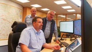 Günter Storch, Leiter der Rettungs- und Feuerwehrleitstelle sowie Kreisbrandmeister Hans-Hermann Fehling (hinten, von links) blicken Ralf Wiechers bei der Arbeit am UnwetterClient über die Schulter.